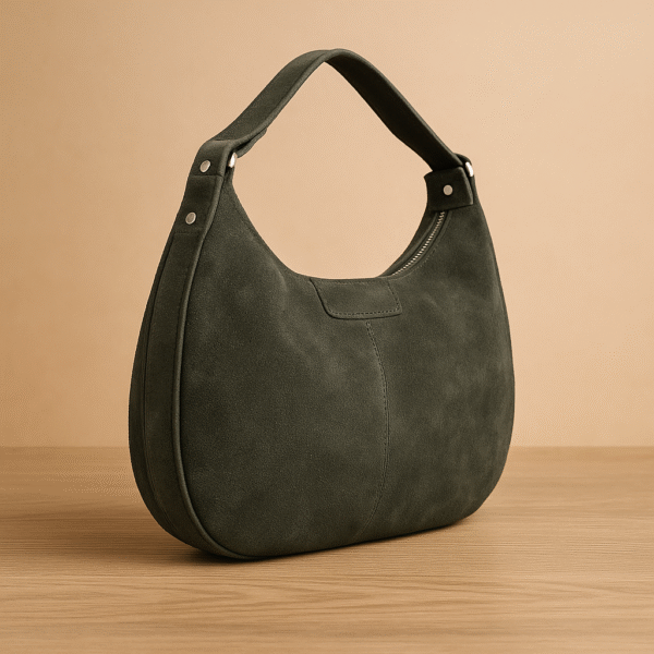 Tamsiai žalia zomšinė moteriška rankinė su plačia rankena ir sidabro detalėmis, pastatyta ant neutralaus fono